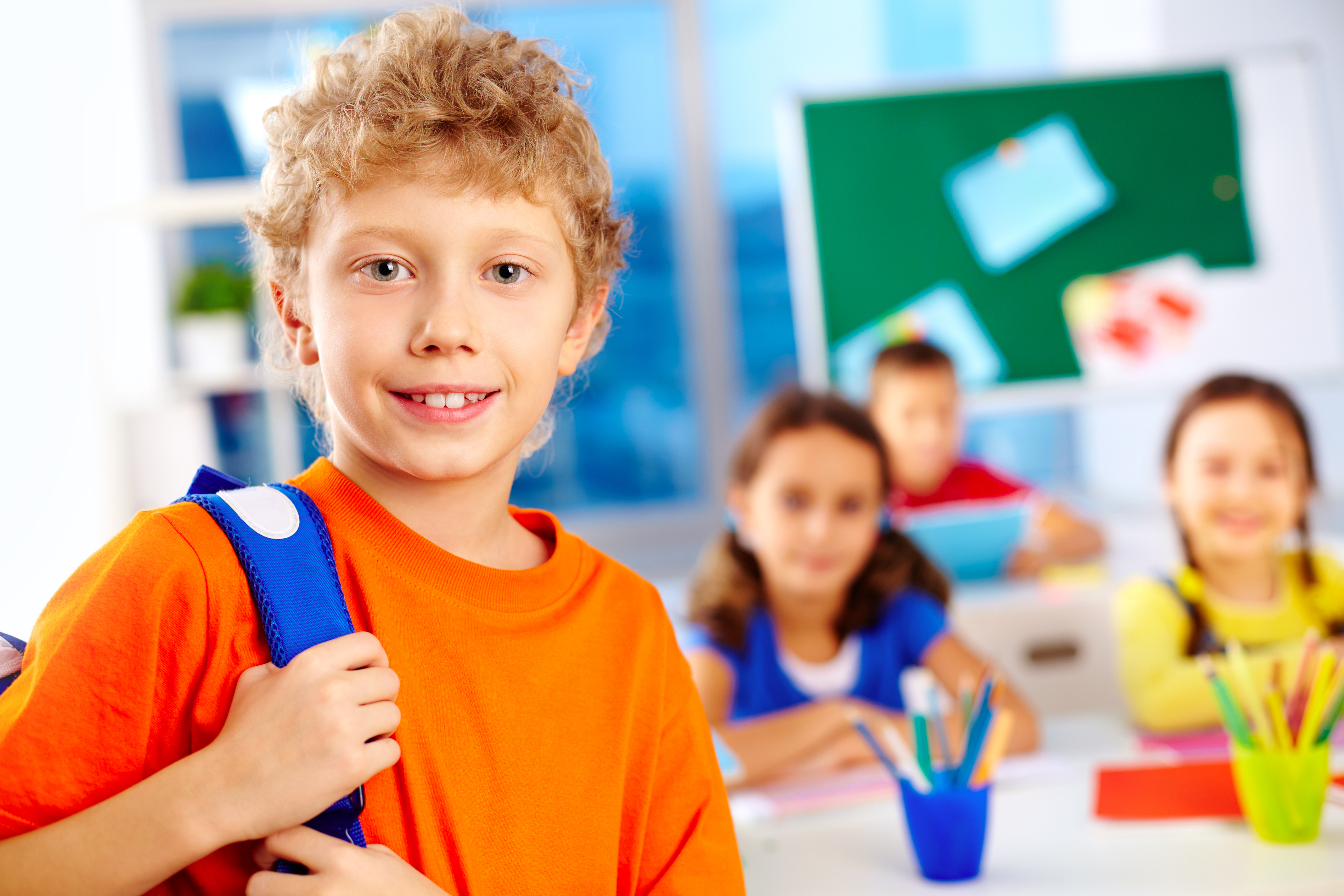 Portrait of cute schoolboy with backpack looking at camera with his classmates on background